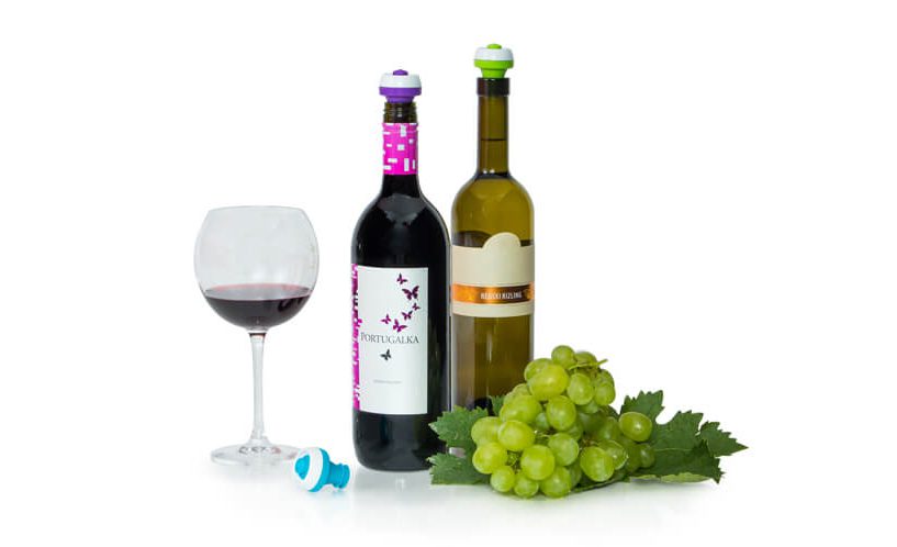 Steklenici vina z vakuumskimi zamaški, natočen kozarec črnine in grozdje na belem ozadju.